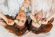 © Daria Lukoiko - Two girls make homemade face and hair beauty masks. Cucumbers for the freshness of the skin around the eyes. Women take care of youthful skin. Girlfriends laugh at home lying on the floor on pillows.