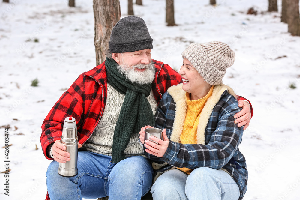 Happy mature couple drinking hot tea in forest on winter day