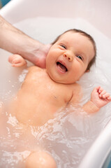 Wall Mural - small child takes a bath. Parents bathe the baby. Pretty Baby. The newborn is bathed. Crusts on the baby's face. Bathroom with milk. The newborn is smiling. Beautiful kid portrait. little child smiles