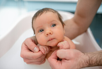 Wall Mural - small child takes a bath. Parents bathe the baby. Pretty Baby. The newborn is bathed. Crusts on the baby's face. Bathroom with milk. The newborn is smiling. Beautiful kid portrait. little child smiles