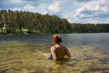 Fototapeta  - Dziewczyna wypoczywająca nad czystym jeziorem w promieniach letniego słońca, w tle zielony las.