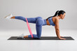 © nikolas_jkd - Fitness woman doing kickback exercise for glutes with resistance band on gray background. Athletic girl working out donkey kicks