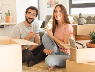 Poster - young couple smiling cheerfully, feeling happy and pointing to the side and upwards, showing object in copy space