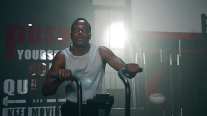 Wall Mural - African ethnicity man listening music while using spinning bike on cardio machine in fitness gym
