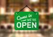 Hanging sign for shop with text Come in we're open on blurred restaurant background.