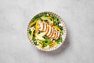 Wall Mural - Easy Grilled Chicken breast salad with mango and avocado slices, sprinkled with walnuts and feta cheese. Spinach and arugula salad. Light gray background. top view. space for text