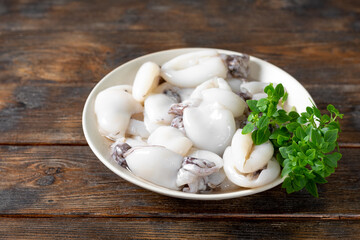 Wall Mural - Raw cuttlefish in a ceramic plate on the kitchen table. Lots of peeled squid in a bowl on a brown wooden table. The concept of cooking shellfish