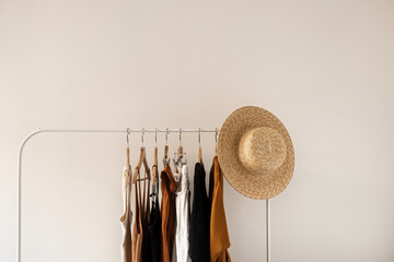 Wall Mural - Aesthetic minimalist fashion influencer blog concept. Summer female dress, tops, t-shirts, straw hat on clothing rack on white wall. Fashion women clothes