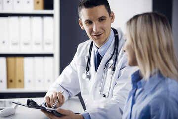 friendly male doctor and patient woman discussing current health examination while sitting in clinic