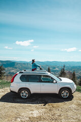 Wall Mural - young woman sitting on the top of the suv car at mountain peak enjoying the landscape view