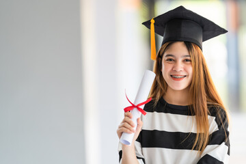 Wall Mural - Young asian woman university graduates in graduation gown and mortarboard holds a degree certificate celebrates education achievement in the university campus.  Education stock photo