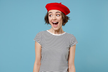 Wall Mural - Young surprised excited caucasian overjoyed woman 20s with short hairdo in french beret red hat striped t-shirt spread hands isolated on pastel blue background studio portrait People lifestyle concept