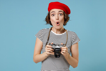 Wall Mural - Young surprised shocked amazed photographer tourist woman with short hairdo in french beret red hat striped t-shirt hold retro vintage photo camera isolated on pastel blue background studio portrait.