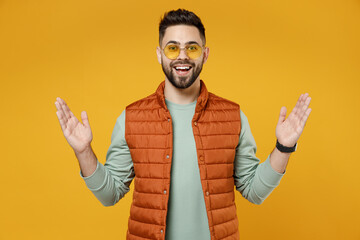 Wall Mural - Young surprised excited happy shocked cheerful fun caucasian man 20s wear orange vest mint sweatshirt glasses spreading hands isolated on yellow background studio portrait. People lifestyle concept.
