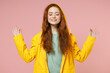 © ViDi Studio - Redhead young woman in yellow waterproof raincoat outerwear hood hold spread hands in yoga om gesture relax meditate try calm down isolated on pink background studio Outdoors wet fall season concept.
