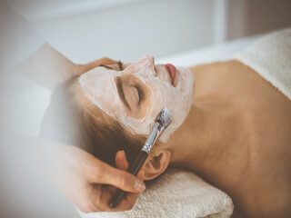 Beautiful brunette woman enjoying applying cosmetic mask with closed eyes comfortable and blissful. Relaxing treatment in medicine and spa center concepts