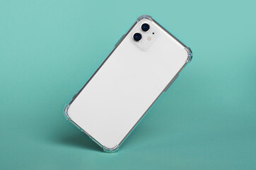 Wall Mural - White iPhone 11 in clear silicone case falls down isolated on green background back view. iPhone 12 case mockup