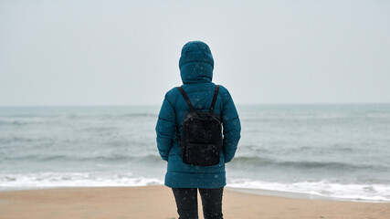 Girl in down jacket standing on seashore in winter