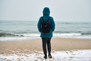 Girl in down jacket standing on seashore in winter