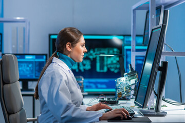 Female microelectronics engineer works in a scientific laboratory on computing systems and microprocessors. Professional electronic factory worker is testing the motherboard and coding the firmware.