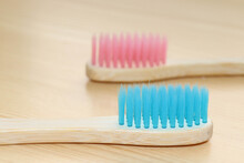 Blue And Pink Bamboo Toothbrushes On A Wooden Background. A Concept For Sustainable And Zero Waste Self-care
