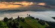 Jamnik, Slovenia - Magical foggy summer morning at Jamnik St.Primoz hilltop church. at sunrise. The fog gently goes behind the small chapel with golden sky and Julian Alps at background