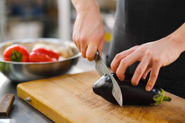 Wall Mural - The male Caucasian chef cuts vegetables, peppers, tomatoes and eggplants on a wooden cutting board.