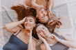 © Daria Lukoiko - Women rest and have fun. Girlfriends laugh at home lying on the floor on pillows. Tree girls make homemade face and hair beauty masks. Women take care of youthful skin.