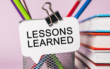 Text LESSONS LEARNED a white sticker with office stationery background. Flat lay on business, finance and development concept