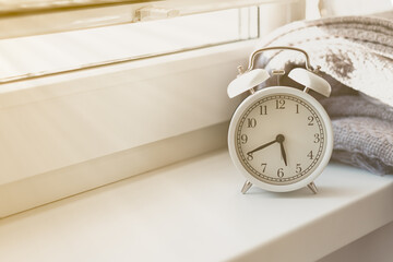 Early morning wake up concept. Retro alarm clock showing five forty five. Bed cover, window, sun light. Good start for efficient and sucessful day. Close up, white background. Copy space for text