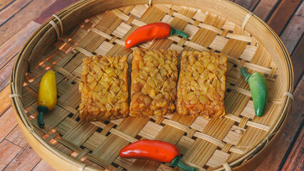 Wall Mural - Fried tempeh decorated with chilies leaves on woven bamboo. selective focus - indonesian food, vegetarian food, soybean product.B