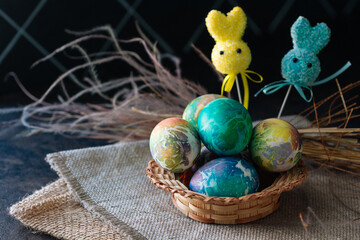 multi-colored Easter eggs of blue tones and two Easter bunny on a stick on a brown cloth background