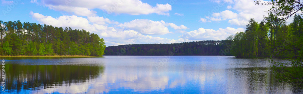 Czyste jezioro położone wśród zielonych lasów. Słoneczny, ciepły dzień, gra świateł i kolorów. - obrazy, fototapety, plakaty 