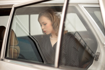 young beautiful girl in a black vintage polka dot dress sitting in a vintage white car