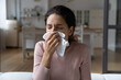 Running nose. Ill latina lady staying at home catching cold rhinitis viral bacterial infection using hygienic one time handkerchief. Young female suffer from seasonal allergy blow nose in paper tissue