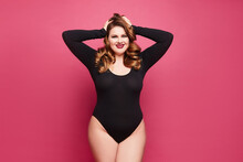 A Young Plus-size Model Woman With Bright Makeup And Full Red Lips Wearing A Black Bodysuit Isolated Over Pink Background