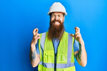 Poster - Redhead man with long beard wearing safety helmet and reflective jacket gesturing finger crossed smiling with hope and eyes closed. luck and superstitious concept.