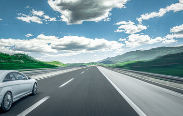 White car rushes along the road against the backdrop of a beautiful countryside landscape.