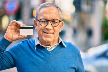 Wall Mural - senior grey-haired man smiling happy holding credit card at the city.