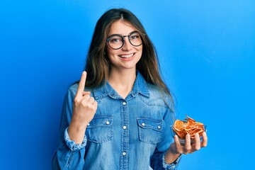 Wall Mural - Young caucasian woman holding bowl of dry orange smiling with an idea or question pointing finger with happy face, number one