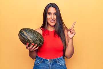 Sticker - Young beautiful brunette woman holding melon smiling happy pointing with hand and finger to the side