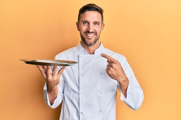 Canvas Print - Handsome man with beard wearing chef uniform holding silver tray smiling happy pointing with hand and finger