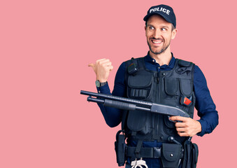 Wall Mural - Young handsome man wearing police uniform holding shotgun pointing thumb up to the side smiling happy with open mouth