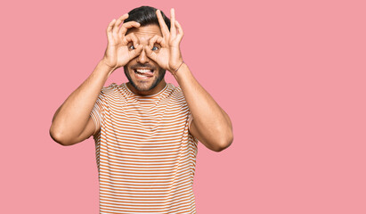 Handsome hispanic man wearing casual clothes doing ok gesture like binoculars sticking tongue out, eyes looking through fingers. crazy expression.