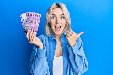 Sticker - Young blonde girl holding philippine peso banknotes pointing thumb up to the side smiling happy with open mouth