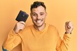 © Krakenimages.com - Young hispanic man holding leather wallet screaming proud, celebrating victory and success very excited with raised arm