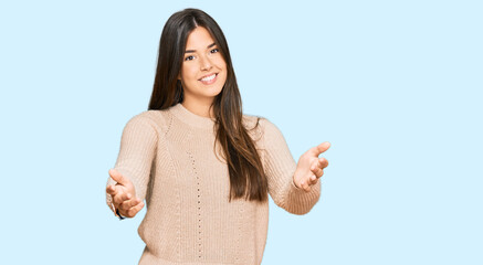 Sticker - Young brunette woman wearing casual winter sweater smiling cheerful offering hands giving assistance and acceptance.