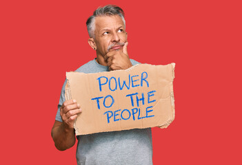 Sticker - Middle age grey-haired man holding power to the people banner serious face thinking about question with hand on chin, thoughtful about confusing idea