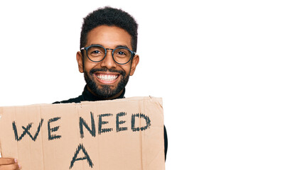 Wall Mural - Young african american man holding we need a change banner celebrating victory with happy smile and winner expression with raised hands