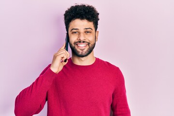 Poster - Young arab man with beard having conversation talking on the smartphone looking positive and happy standing and smiling with a confident smile showing teeth